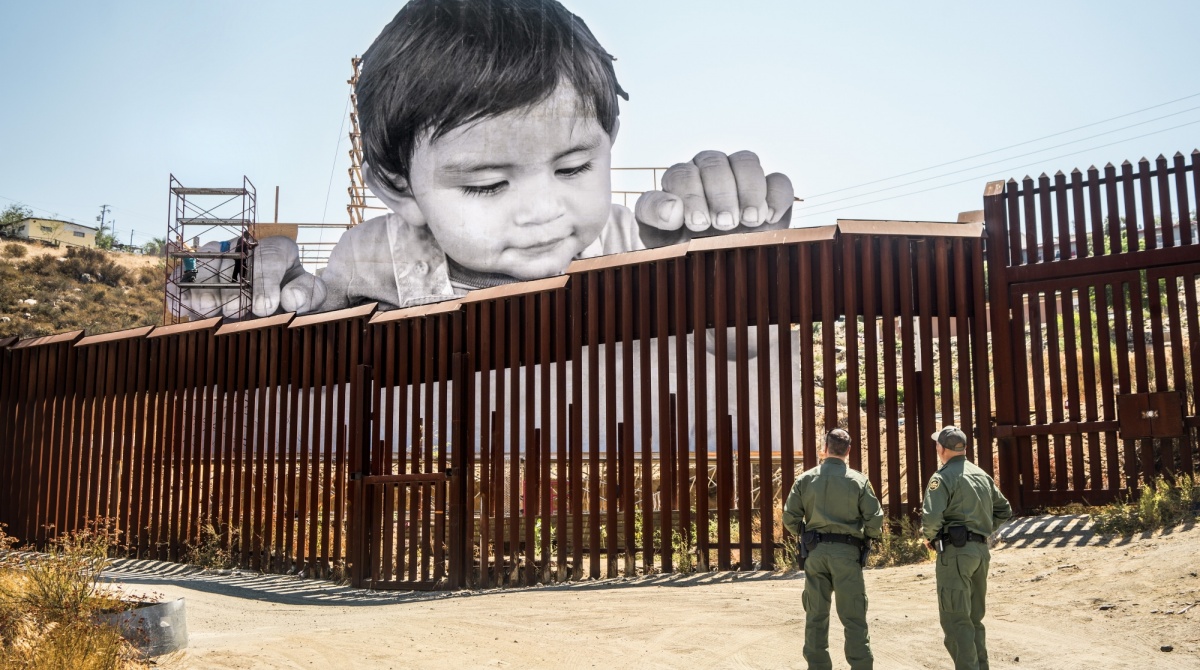 JR (French, born 1983). GIANTS, Kikito and the Boarder Patrol, Tecate, Mexico—U.S.A., 2017. Installation image. Wheat-pasted poster. ©️ JR-ART.NET